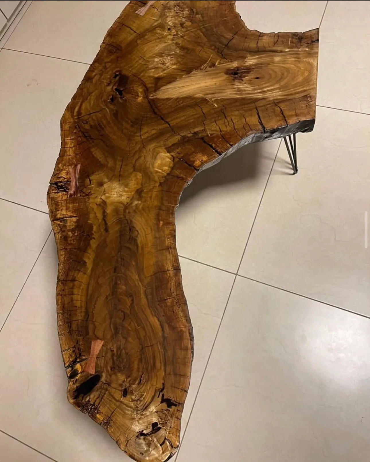 Mesa de centro feita de uma prancha de madeira de borda viva e formato irregular, apoiada em pés finos de ferro preto, numa sala de piso claro. — foto 2