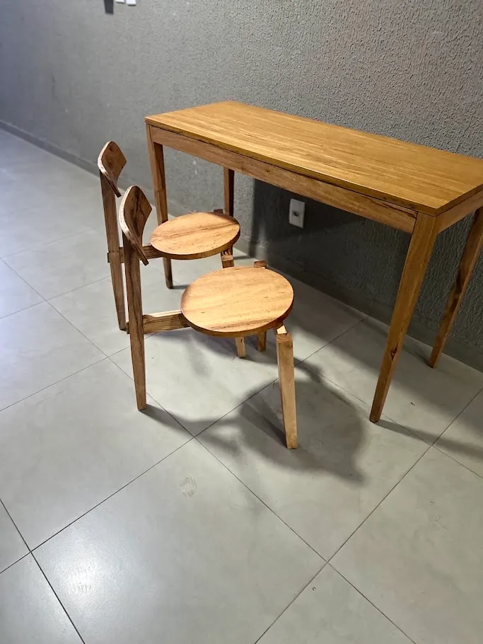 Mesa estreita de madeira maciça encostada na parede de uma cozinha, posta para duas pessoas, com duas cadeiras de assento redondo e encosto curvo. — foto 3