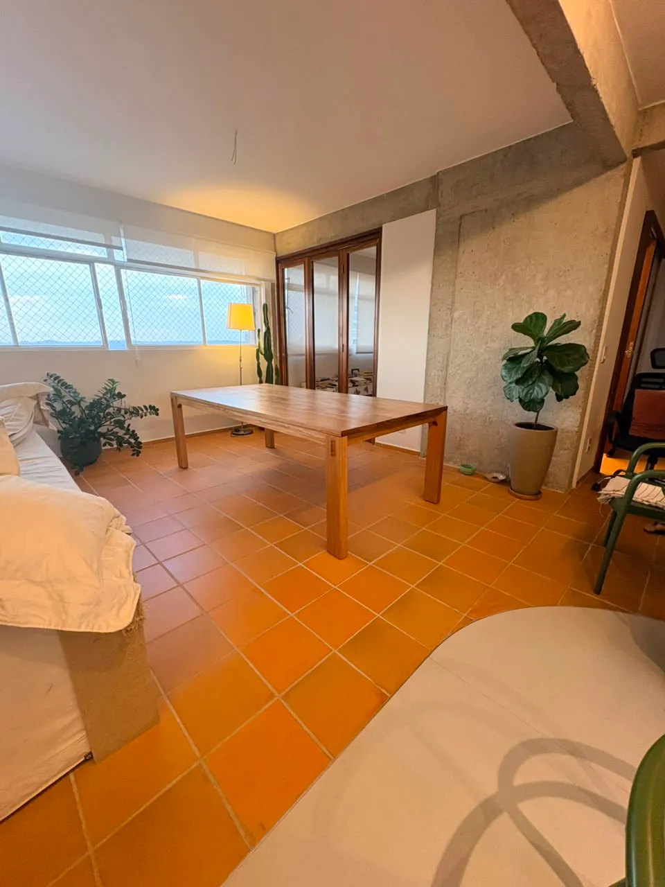 Mesa de jantar retangular em jequitibá-rosa, de pernas quadradas com cavilhas escuras aparentes, sobre piso de cerâmica laranja, entre uma janela e uma parede de concreto aparente. — foto 6