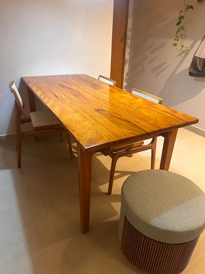 Mesa de jantar retangular em madeira maciça clara, com cadeiras de palhinha em volta, em uma sala de jantar.